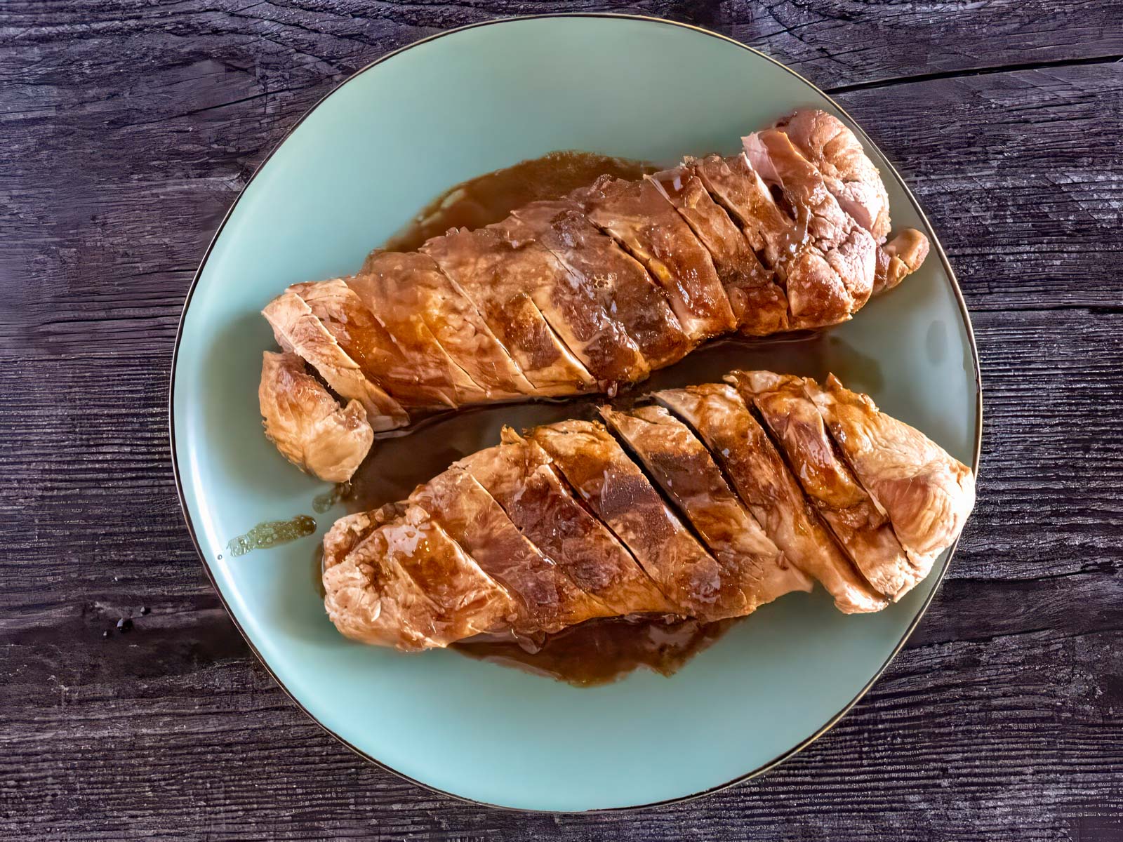 Sliced pork tenderloin with sauce poured over, on a plate