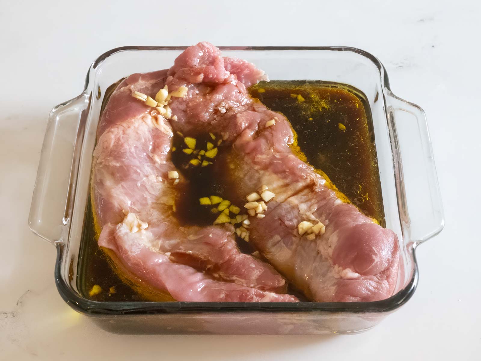 Uncooked pork in dish with marinade poured over top