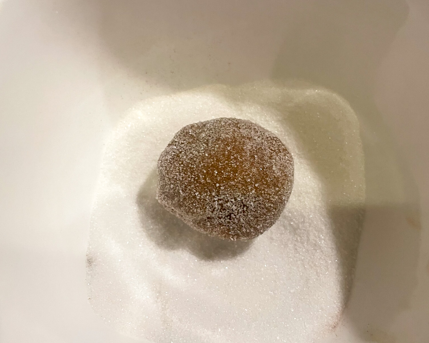 One uncooked cookie being coated in white sugar
