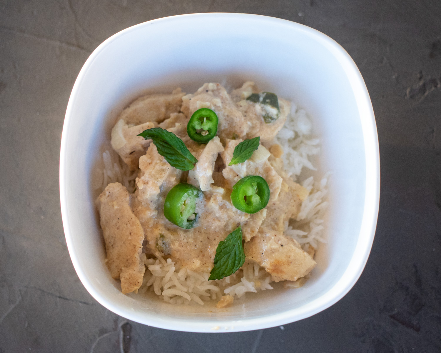 White Chicken Korma in a white bowl, with mint leaves and pepper slices for garnish