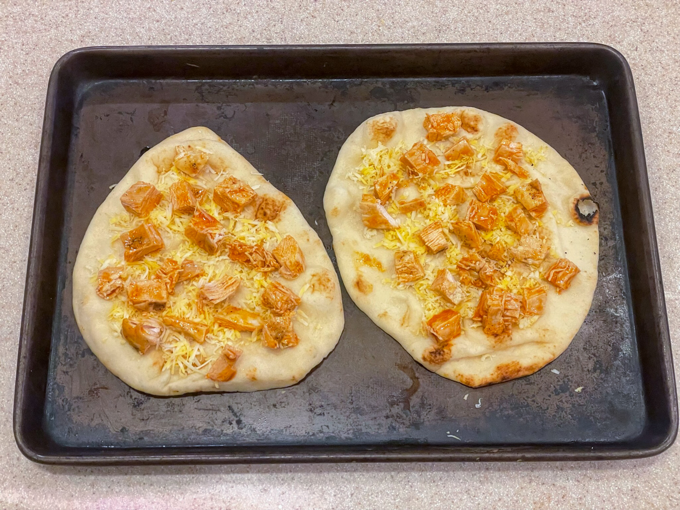 Buffalo-coated chicken placed on top of flatbread and cheese, just before baking