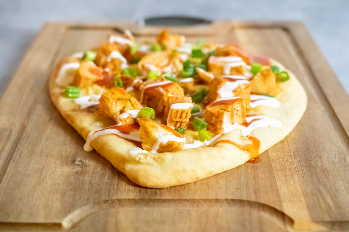 Buffalo chicken flatbread being served on a wooden cutting board
