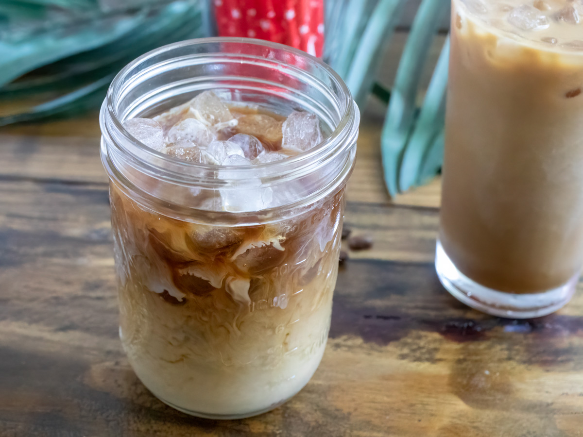 Chick-fil-A Iced Coffee in a mason jar glass, with another glass of coffee and a glass full of red straws in the background