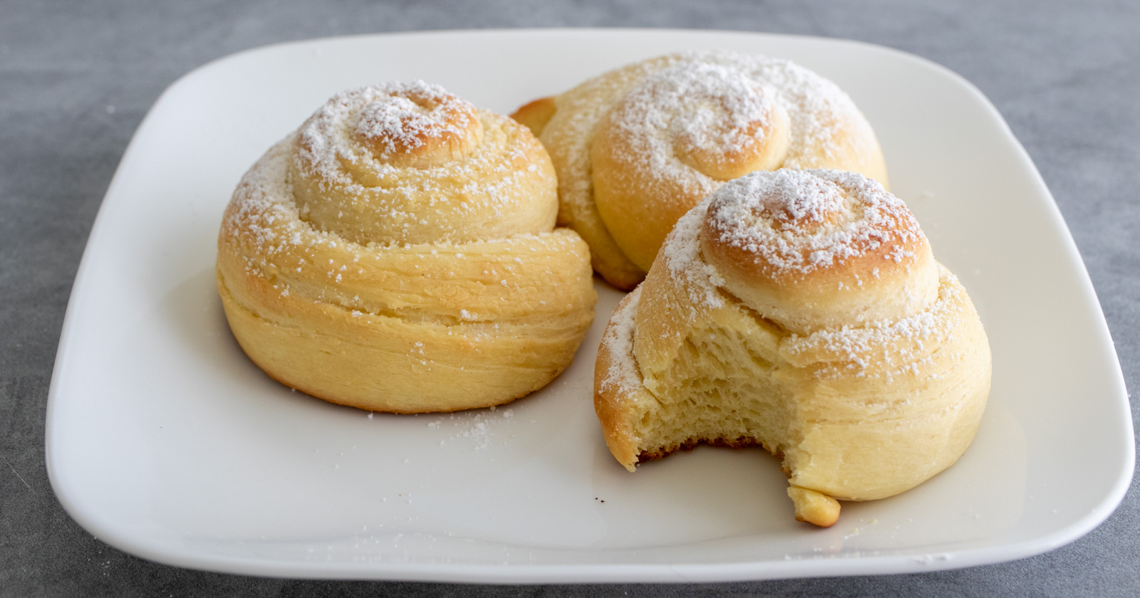 Three pan de mallorca rolls, one with a bite taken out