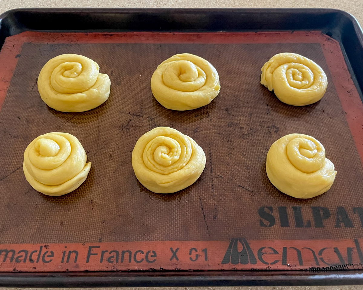 All six pastries after spiral shaping is complete, resting on a silicone baking mat.