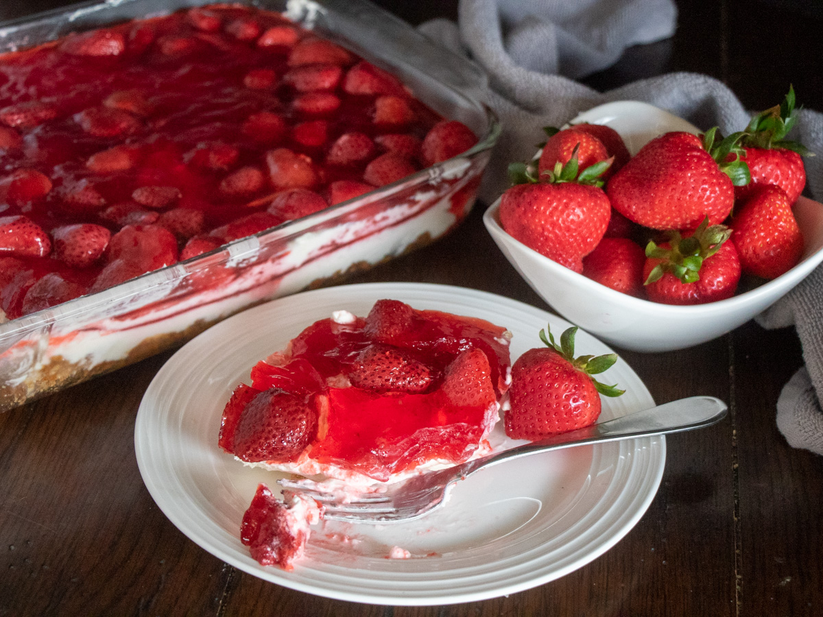 Strawberry pretzel salad with one serving on a plate and beside a bowl of strawberries