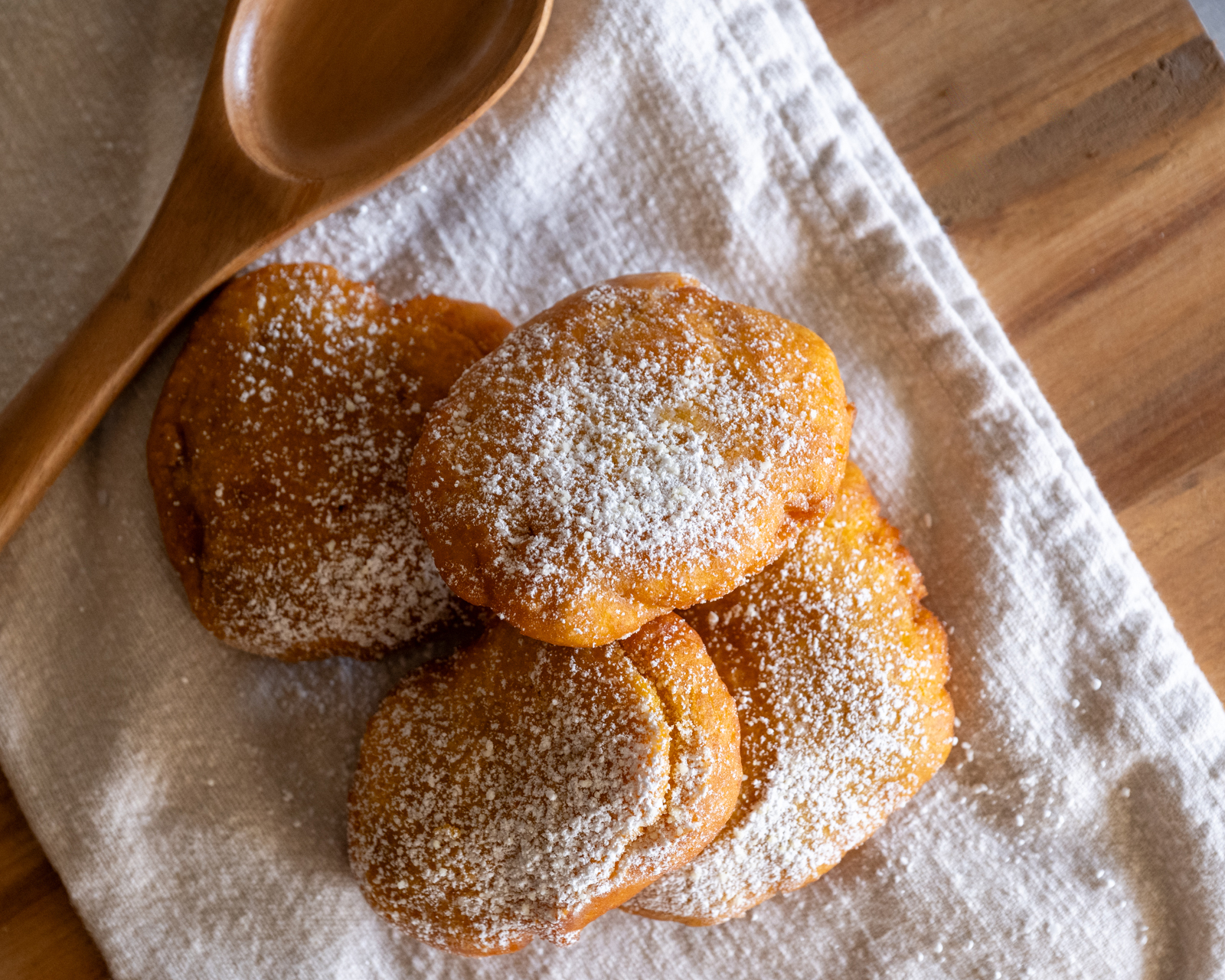 Overhead view of pieces of pumpkin fry bread on a cloth napkin with a wooden spoon, on a cutting board