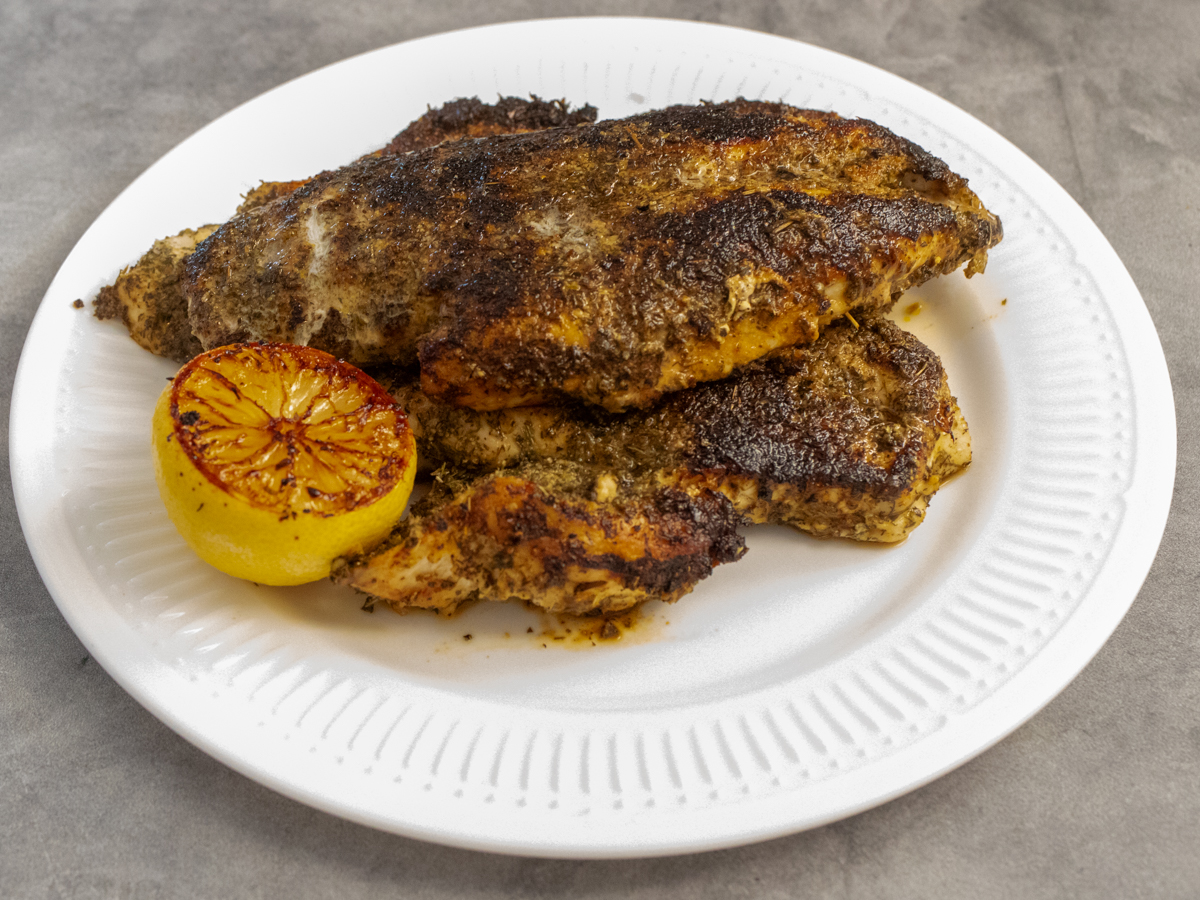 Several pieces of herb crusted chicken arranged on a white plate with half a roasted lemon