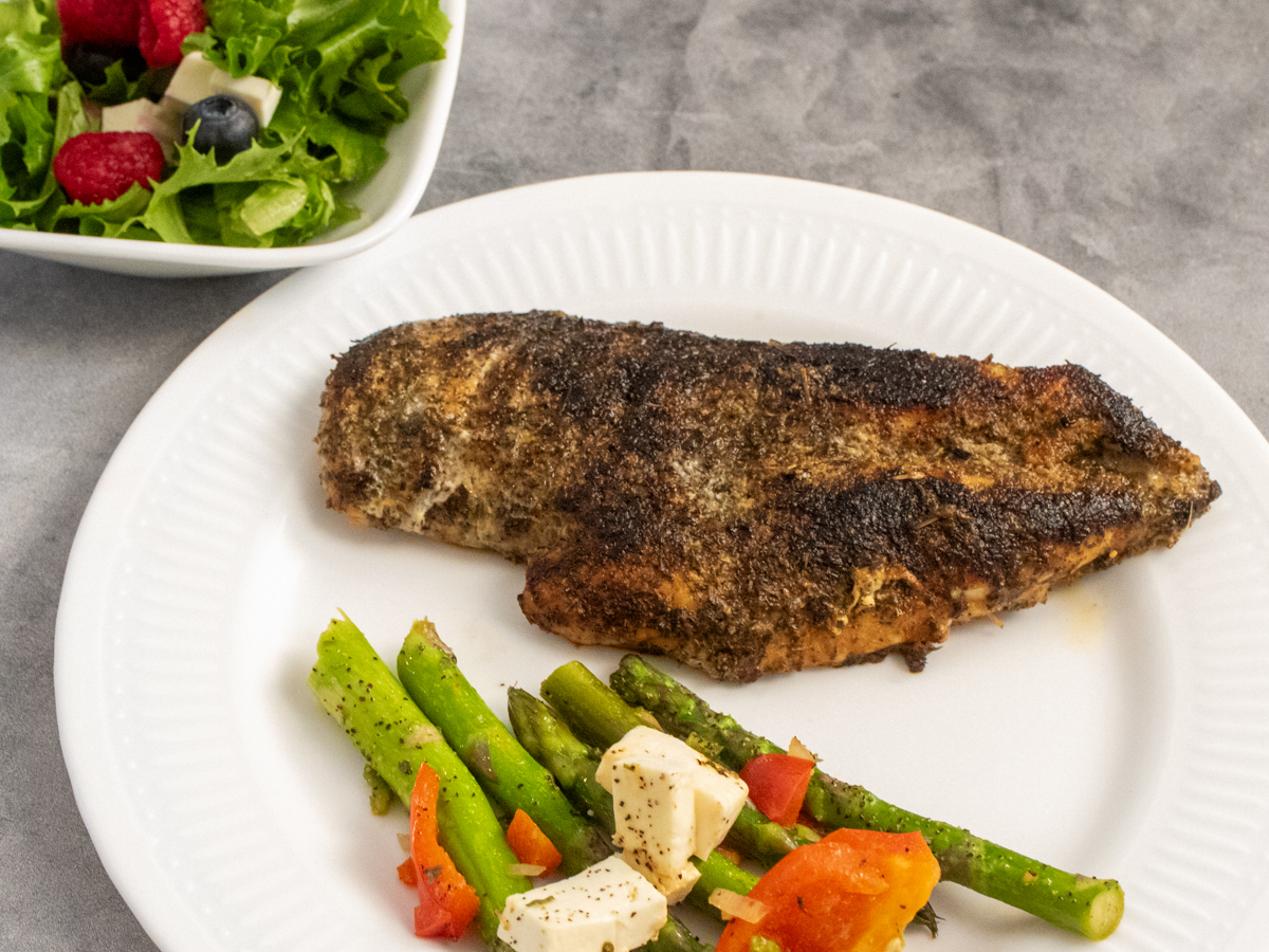 Plated herb crusted chicken with a side dish of asparagus and peppers and a small salad