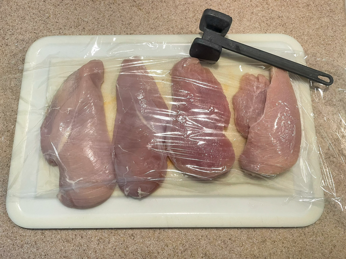 Chicken covered with plastic wrap and ready to be tenderized