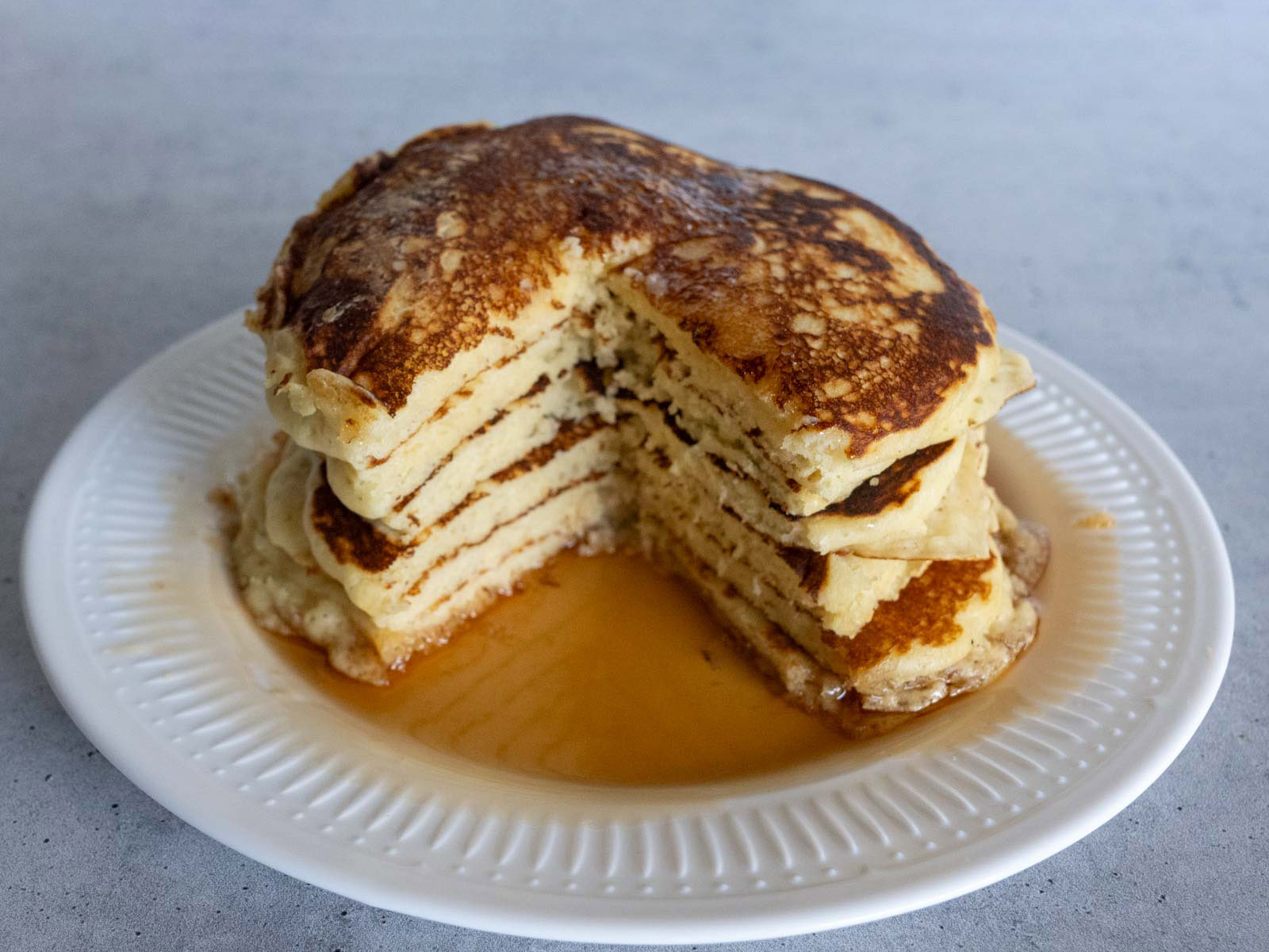 A stack of pancakes swimming in syrup, with a section cut away to show the inside.