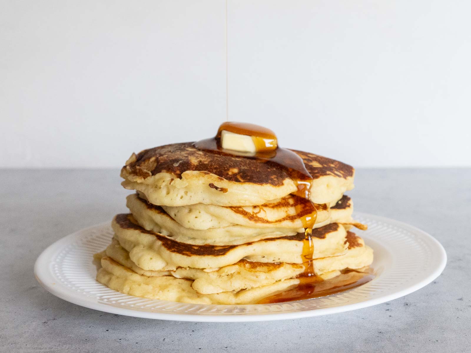 A stack of pancakes with a pat of butter on top, with maple syrup being poured over them